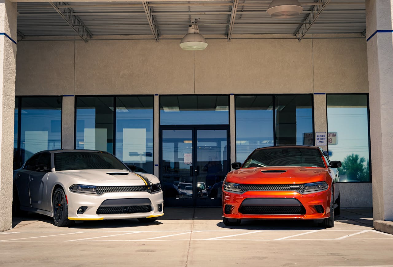 Two Dodge muscle cars parked outside a modern urban dealership entrance.